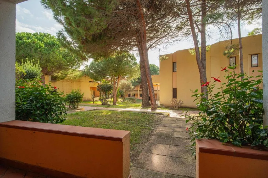 Vialetto del giardino con pini e vegetazione mediterranea tra gli edifici color sabbia