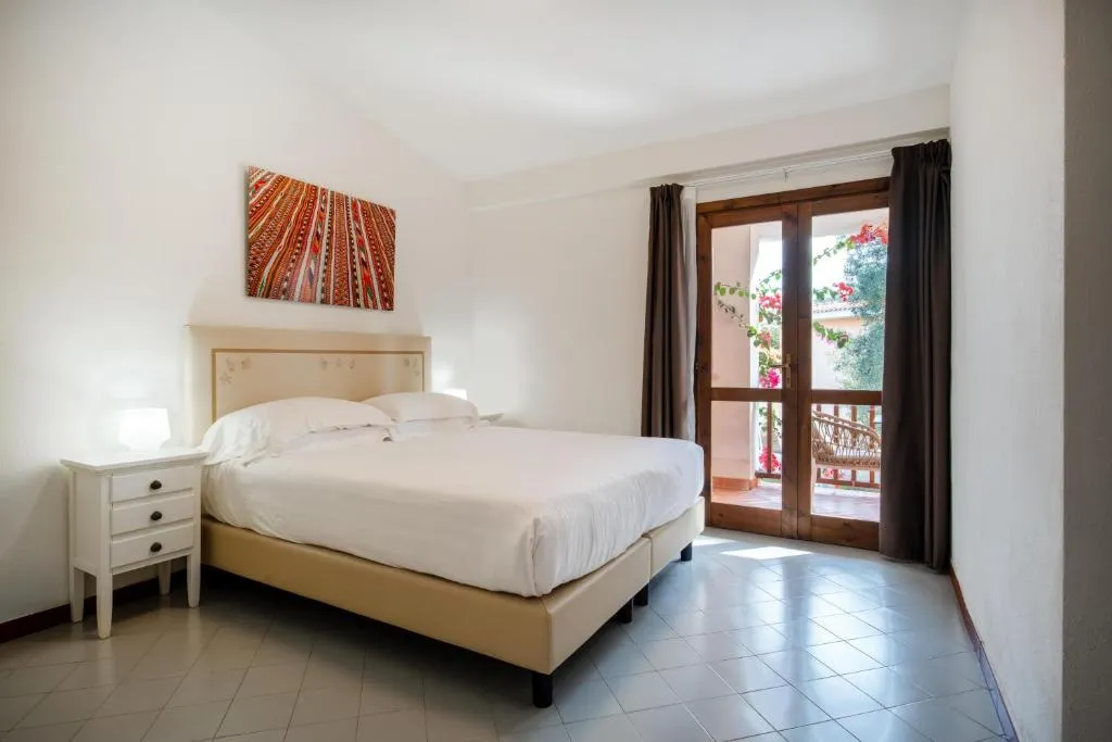 Camera matrimoniale con letto, comodino bianco e porta finestra che si apre sul balcone