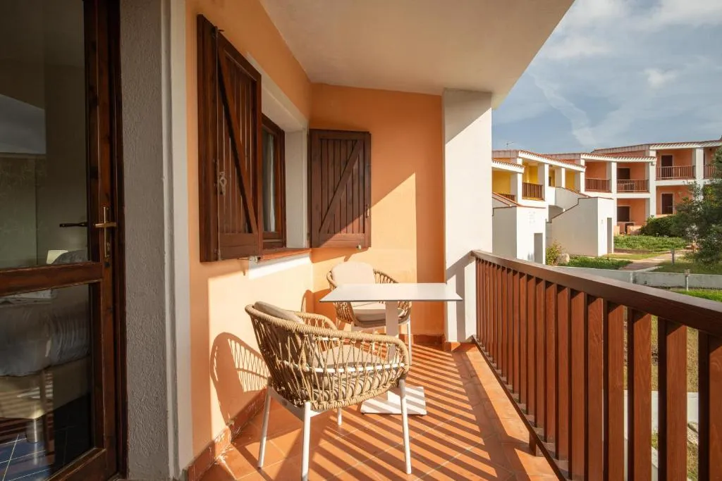Balcone soleggiato con tavolino e poltrone in vimini affacciato sugli edifici del resort