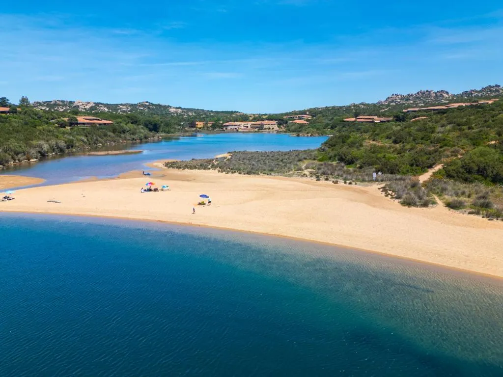 Spiaggia di sabbia dorata tra la laguna e il mare con colline verdi sullo sfondo