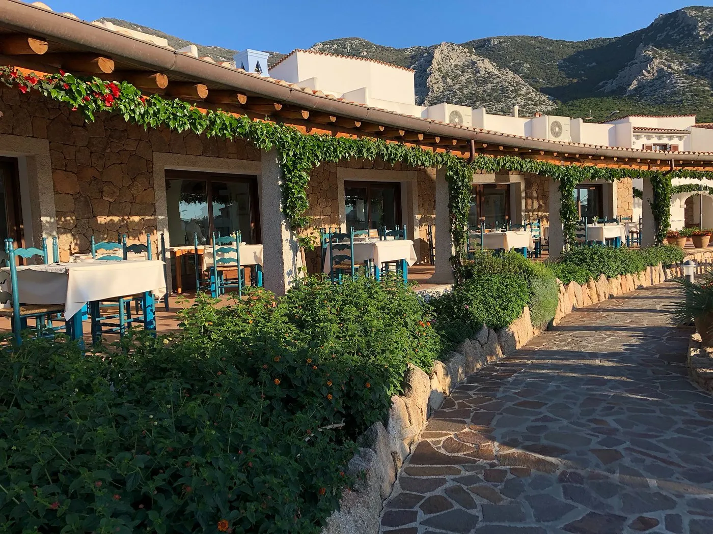 Terrazza ristorante esterna con tavoli apparecchiati e sedie azzurre, sfondo montano
