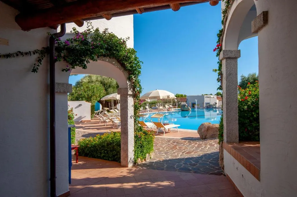 Vista della piscina attraverso archi bianchi con bouganville e lettini