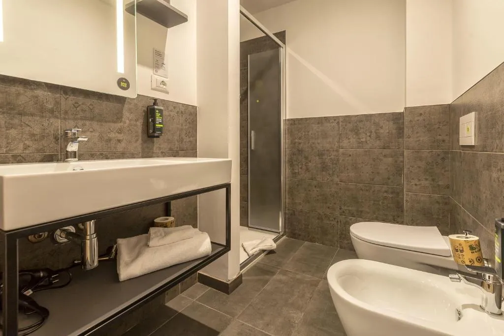 Bagno con lavabo, doccia, WC e bidet e pareti piastrellate grigie
