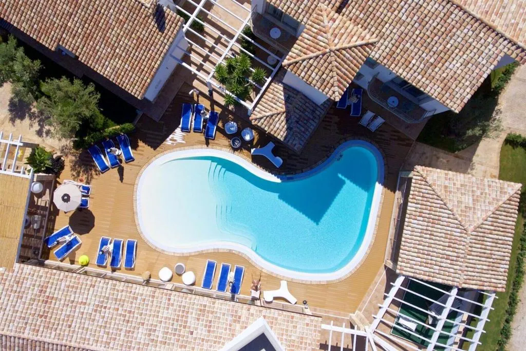 Vista aerea della piscina sagomata con lettini blu tra i tetti in tegole