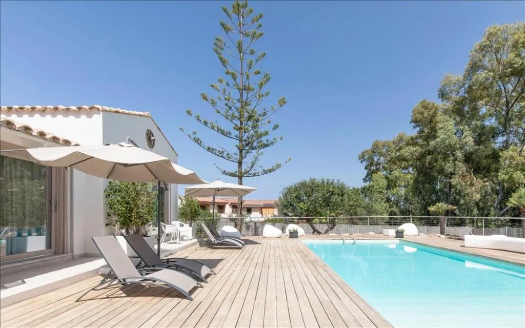 Piscina esterna con lettini e ombrelloni su terrazza in legno tra gli alberi