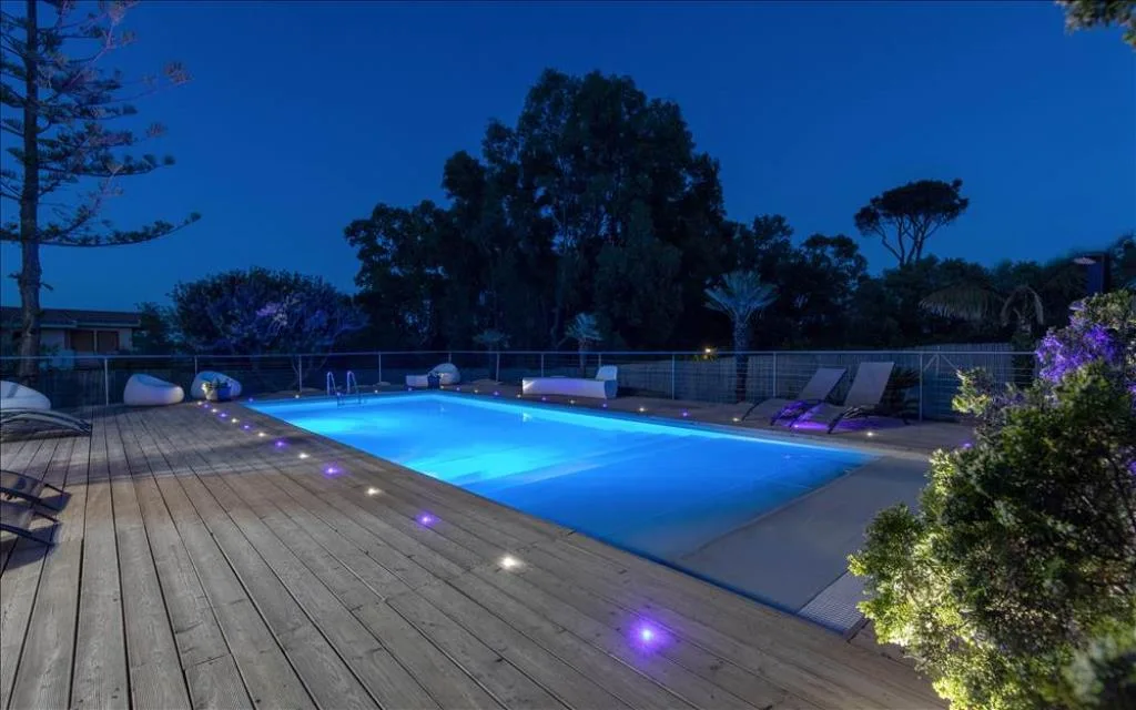Piscina illuminata al crepuscolo con luci blu e viola sulla terrazza in legno