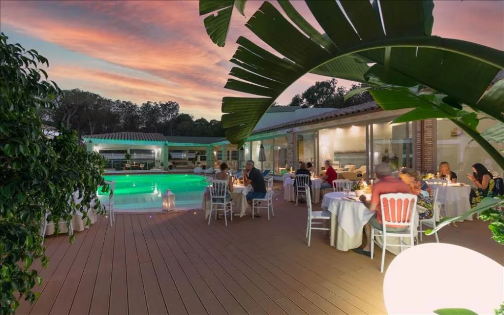 Ospiti a cena all'aperto vicino alla piscina illuminata al tramonto