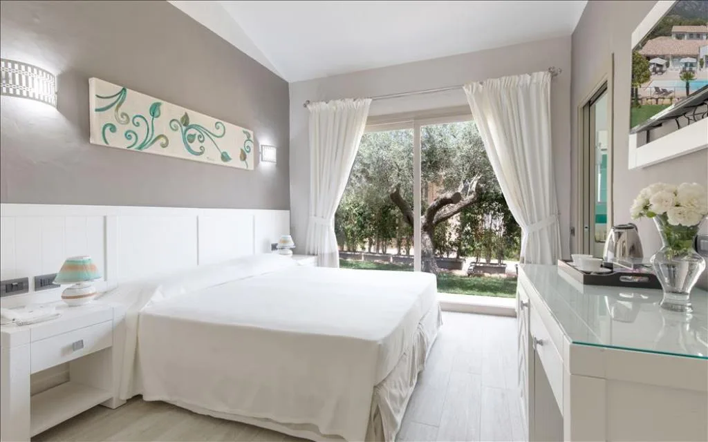 Camera elegante con letto matrimoniale bianco e vetrata sul giardino con ulivi
