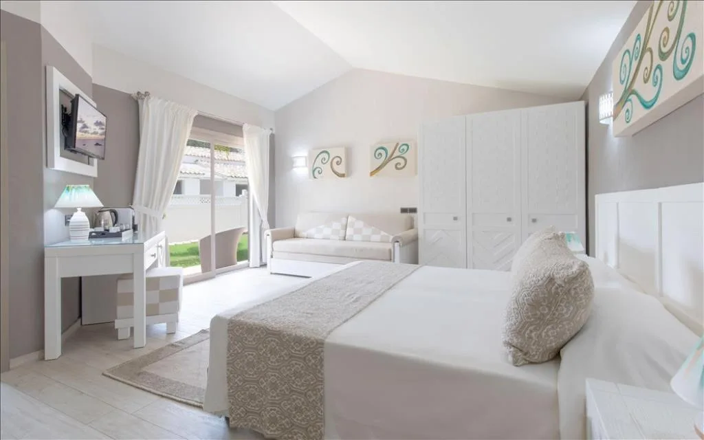 Camera spaziosa bianca con letto matrimoniale, divano e accesso al giardino