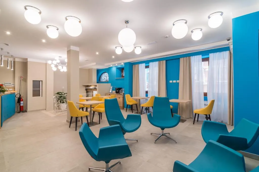 Sala colazione con poltrone blu, sedie gialle, tavoli e lampade a globo