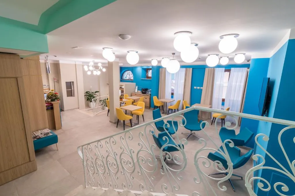 Sala comune con poltrone blu e gialle, tavoli e ringhiera bianca decorata