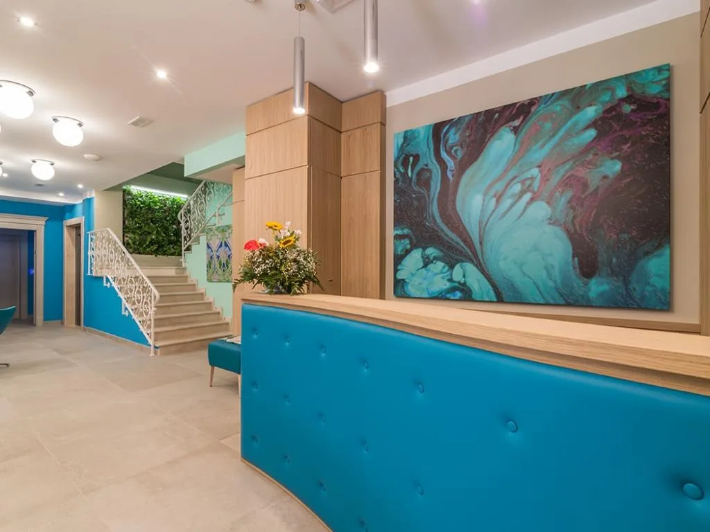 Reception dell'hotel con bancone blu, quadro astratto e scala con ringhiera bianca decorata
