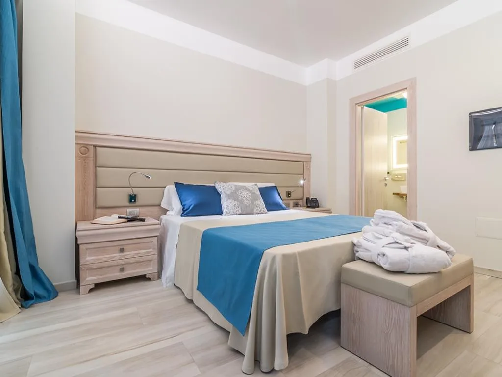 Camera matrimoniale luminosa con biancheria blu, accappatoi e comodini in legno chiaro
