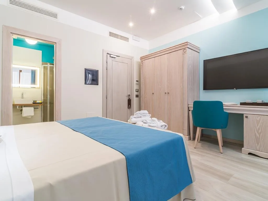 Camera matrimoniale con parete azzurra, scrivania, sedia turchese e bagno con doccia