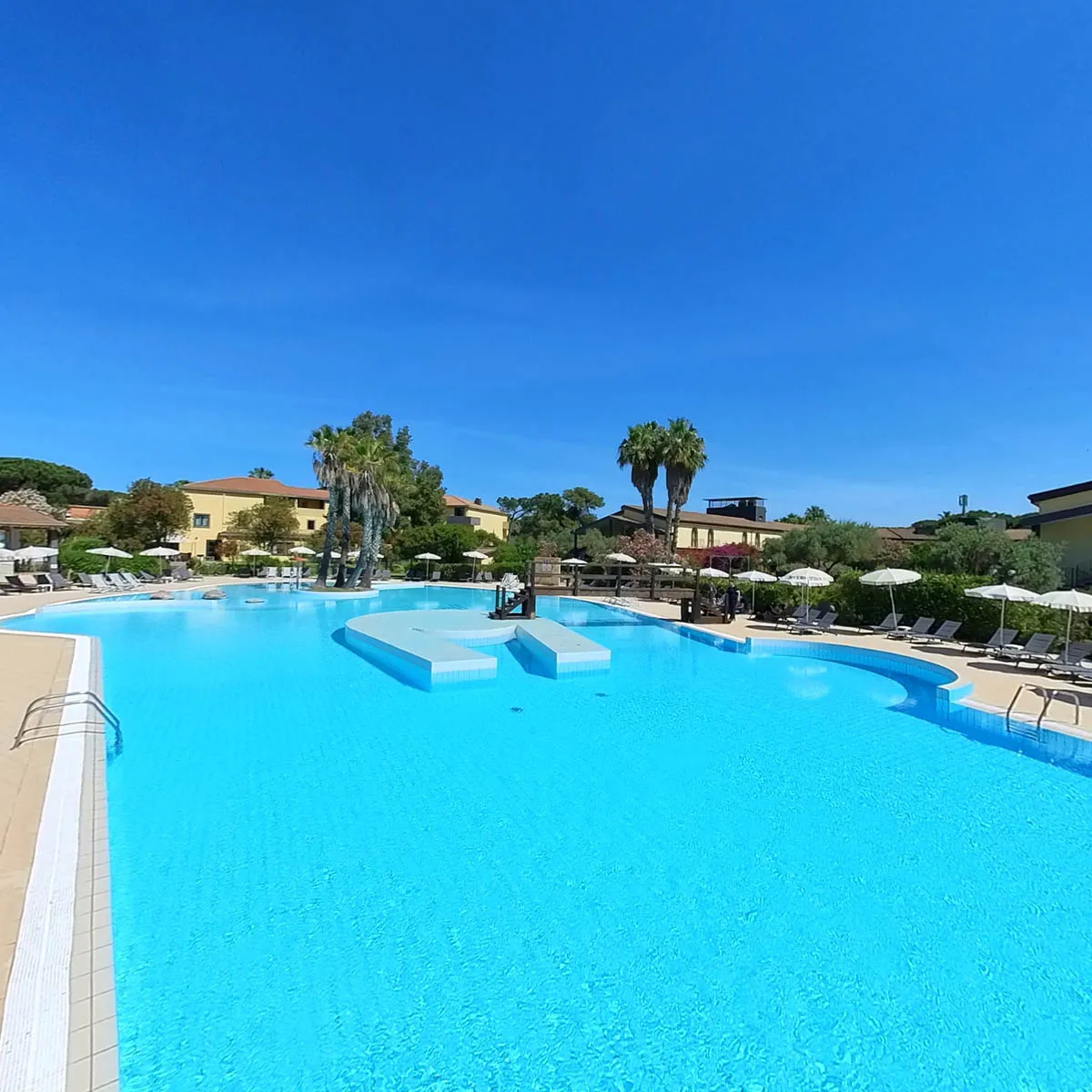 Ampia piscina a forma libera con acqua cristallina, palme ed edifici dell'hotel sullo sfondo