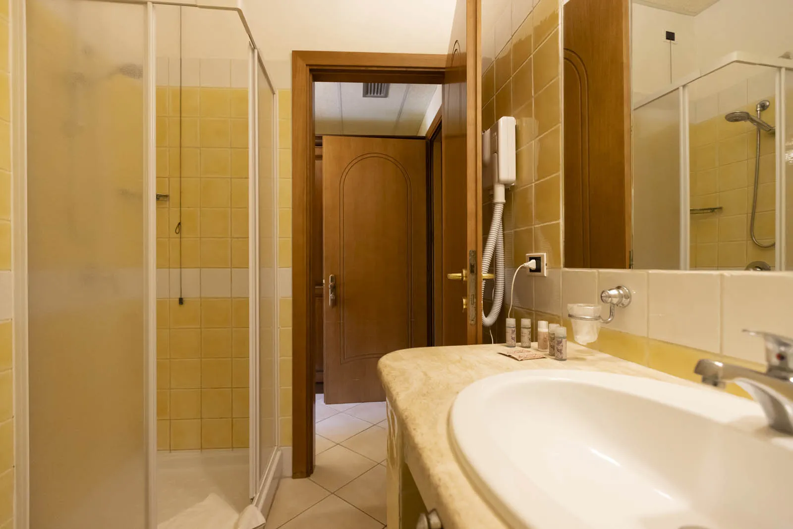 Bagno con piastrelle gialle, doccia, lavabo in marmo e specchio