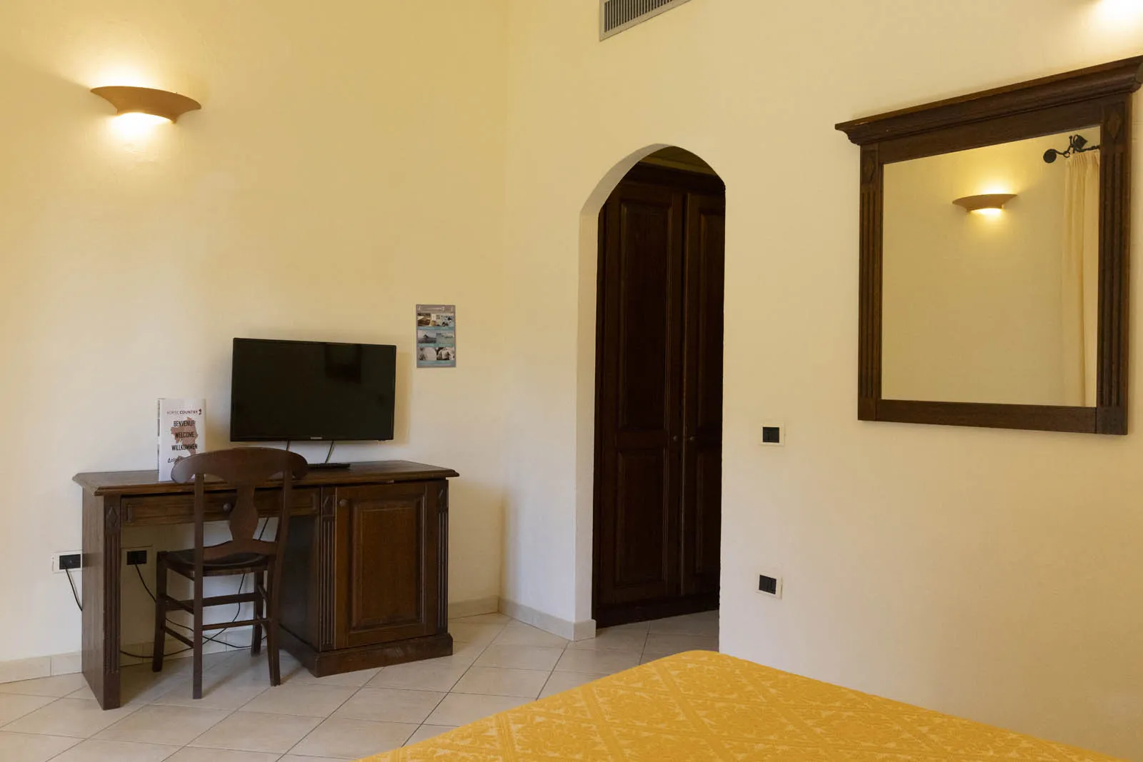 Dettaglio camera con scrivania in legno, TV, specchio e armadio
