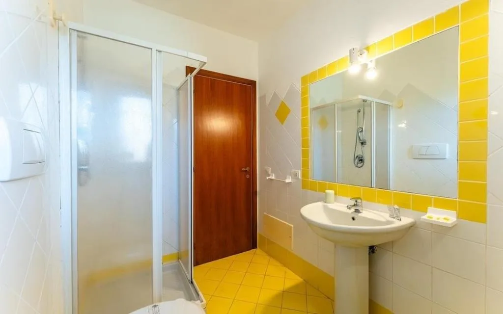 Bagno con doccia, lavabo a colonna e piastrelle gialle e bianche