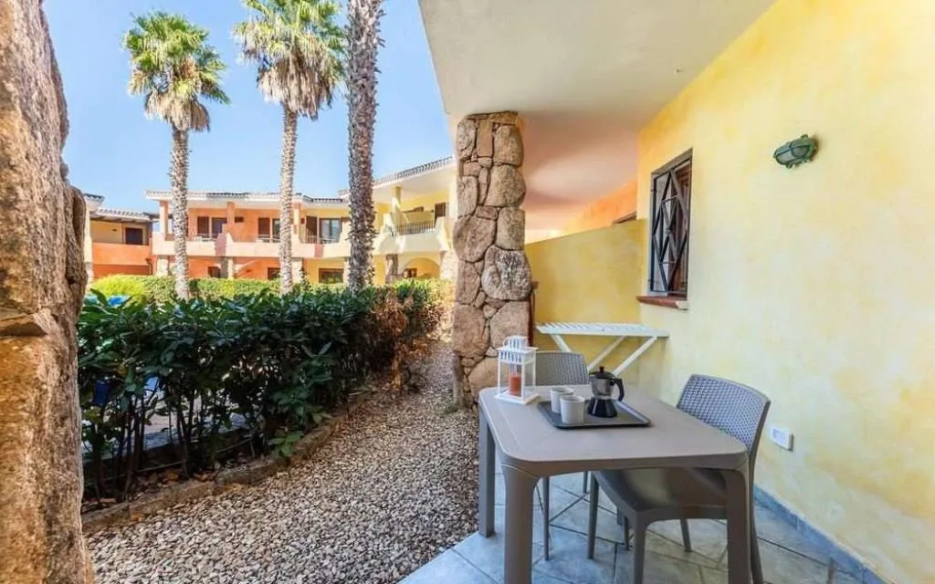 Patio esterno con tavolo e sedie affacciato sul giardino e sugli edifici gialli