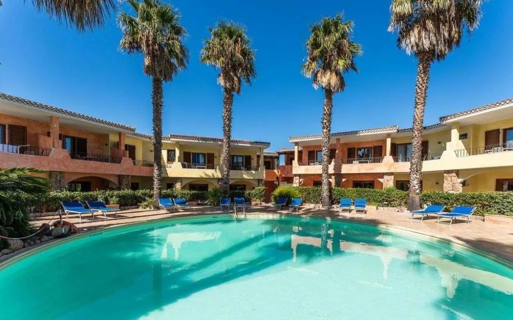 Piscina del residence con palme e appartamenti color giallo e arancio