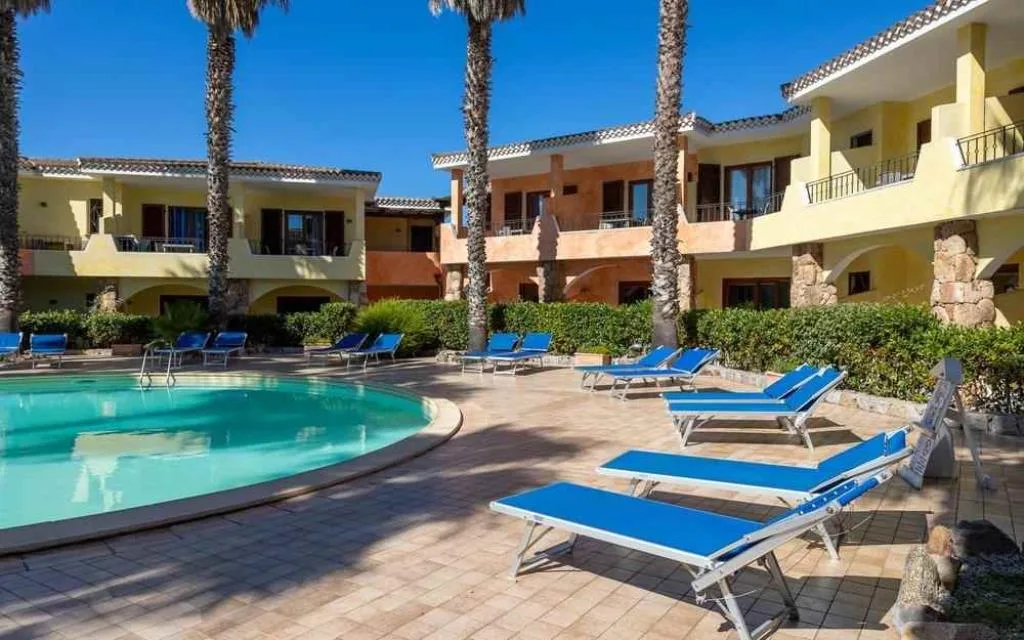 Piscina con lettini blu e palme davanti agli appartamenti gialli