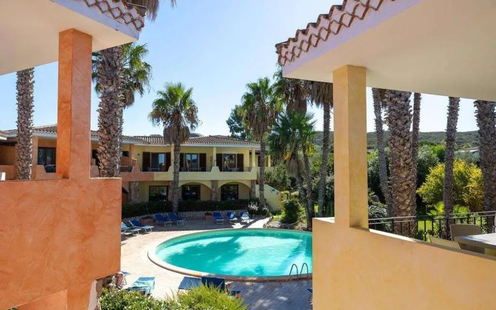 Vista della piscina rotonda tra le palme e gli edifici del residence