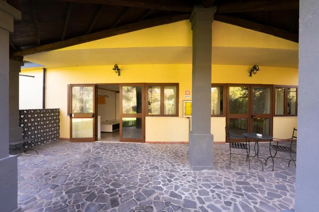 Portico esterno con parete gialla, soffitto in legno, pavimento in pietra e tavolino con sedie in ferro