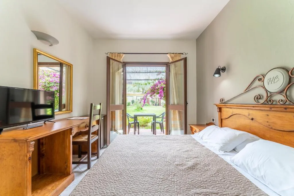 Camera da letto con scrivania in legno, TV, specchio e porta finestra affacciata sul giardino