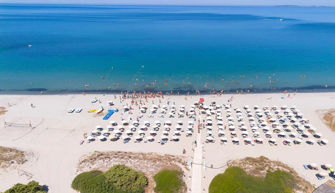 Vista aerea della spiaggia sabbiosa con file di ombrelloni e mare azzurro cristallino