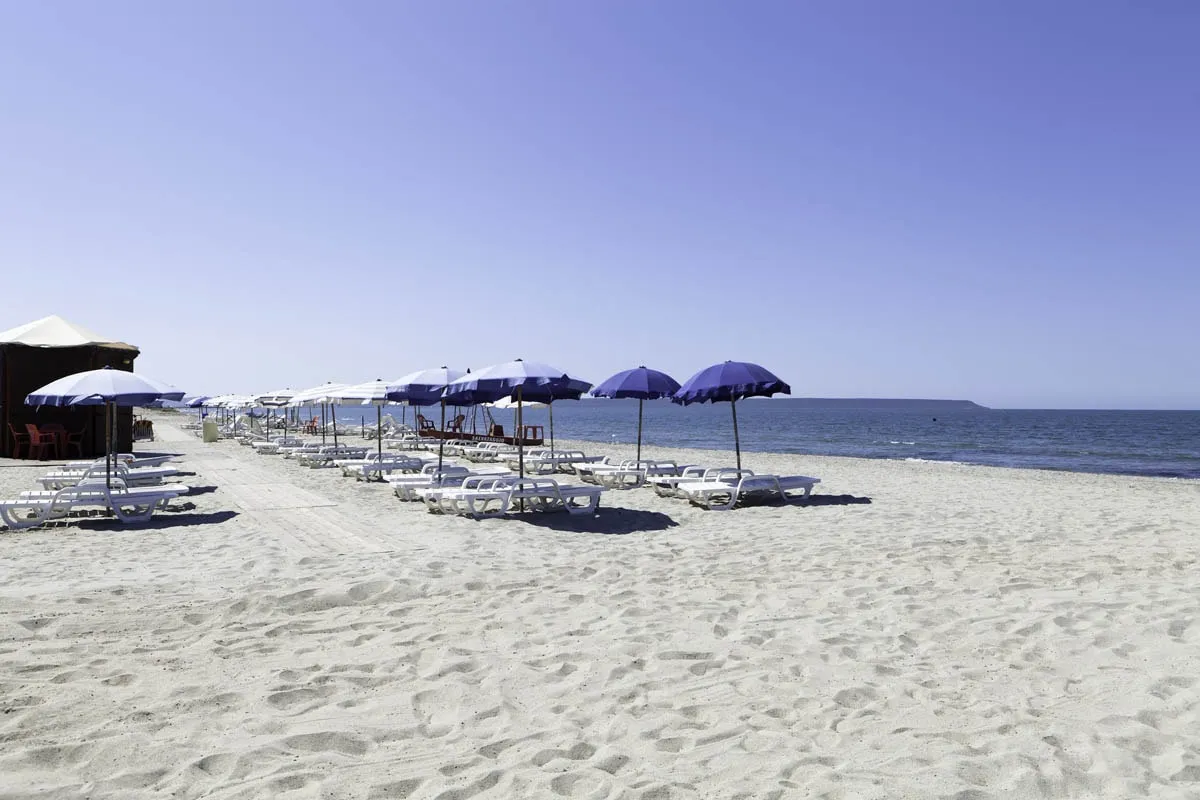 Spiaggia di sabbia bianca con lettini bianchi e ombrelloni blu affacciati sul mare